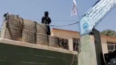 A fighter stands guard next to a Taliban flag raised at the gates outside the police headquarters, in city of Ghazni, Afghanistan in this screen grab taken from a video released by the Taliban on August 12, 2021. Taliban Handout/via REUTERS