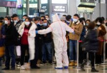 A security guard blocks an exit as he directs people to scan a QR code to track their health status at Shanghai Hongqiao Railway Station
